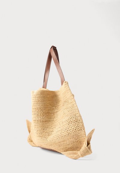 Μπεζ υφαντό τσάντα ώμου με δύο καφέ δερμάτινους ιμάντες και κόμπους στις γωνίες, σε απλό ανοιχτόχρωμο φόντο.