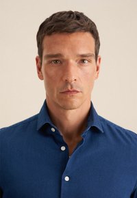 Camicia button-up blu scuro con colletto classico, realizzata in un tessuto liscio. Presenta una vestibilità tailored e bottoni bianchi.