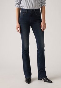 Dark blue denim flared jeans with a mid-rise waist. Features five pockets, subtle fading, and a fitted silhouette down to the knee.
