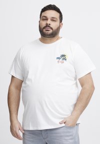 Bílý bavlněný tričko s malým, barevným designem palmy na levé straně hrudi. Volný střih s krátkými rukávy a kulatým výstřihem.