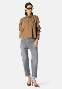 Bruine button-up shirt, grijze versleten spijkerbroek en laarzen met luipaardprint. Geaccessoireerd met oversized gele zonnebril en opvallende oorbellen.