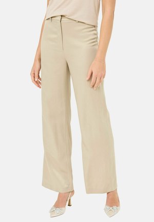Beige wide-leg trousers in smooth fabric; features a front crease, side pockets, and a tailored waistband. Worn with embellished heels.