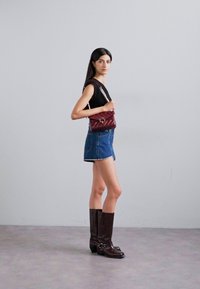 Burgundi värvi pargitud crossbody kott kettstrapiga, millel on ringikujuline riistvaraga aksent, koos musta toppi ja denimpükstega. Pruun nahkking.