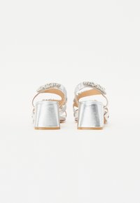 Sølvhevede sandaler med en blank finish, der har blokhæle og dekorative rhinstenbånd på stropperne.