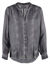 Blusa di seta grigia con una leggera lucentezza, presenta un colletto alla coreana, chiusura frontale con bottoni e due tasche laterali. Maniche lunghe con polsini elastici.