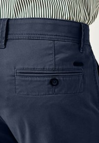 Marineblaue Hosen zeichnen sich durch einen diagonal strukturierten Stoff, eine Gesäßtasche mit einem Knopfverschluss und ein schlichtes Design des Taillenbunds aus.