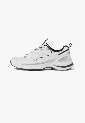 Scarpa da ginnastica bianca con dettagli neri, pannelli in mesh e suola texturizzata, vista laterale su sfondo bianco.