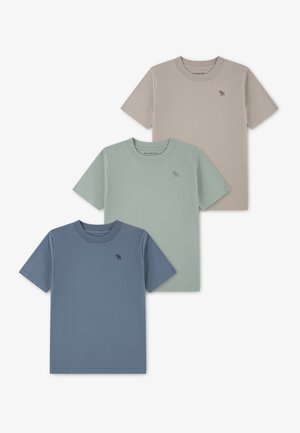 Τρία μονόχρωμα κοντομάνικα t-shirts σε μπεζ, ανοιχτό πράσινο και μπλε, το καθένα με μικρό λογότυπο στο αριστερό στήθος.