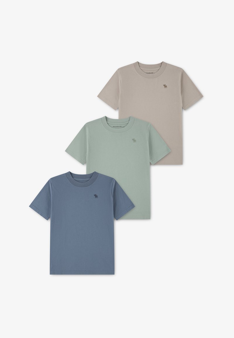 Τρία μονόχρωμα κοντομάνικα t-shirts σε μπεζ, ανοιχτό πράσινο και μπλε, το καθένα με μικρό λογότυπο στο αριστερό στήθος.