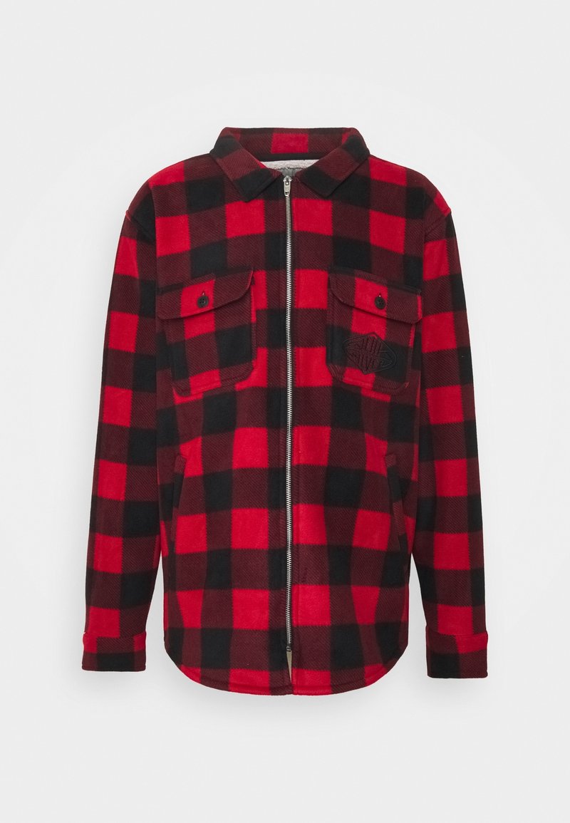Veste à carreaux rouges et noirs avec manches longues, fermeture éclair à l'avant, deux poches poitrine à boutons et un col sur un fond uni.
