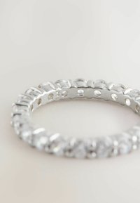 Bague en argent ornée de strass, présentant un design circulaire avec des pierres grandes et petites alternées, un fini métal poli et des côtés ouverts.