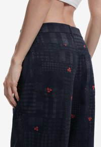 Tmavomodré nohavice z látky s mriežkovým vzorom a malými červenými čerešňami. Obsahujú dve zadné vrecká a vysoký pás.