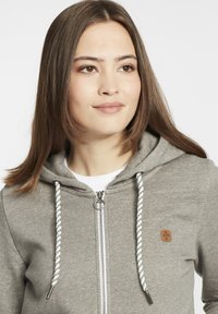 Siva zip-up dukserica napravljena od teksturiranog materijala, s prednjim patentnim zatvaračem, vezicama sa pletenim uzorkom i malim logom.