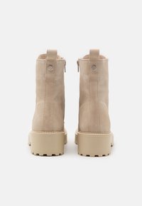 Beige ankelstøvler i ruskind med en tekstureret overflade, rund tå, lynlåslukning og en kraftig beige sål med rillet detaljer.