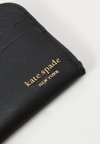 Black textured card case featuring a gold "kate spade NEW YORK" logo. Includes slots for cards and a slim design.