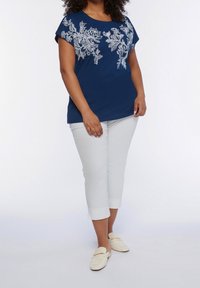 Mörkblå kortärmad topp med vit blommönsterbroderi, tillsammans med beskurna vita byxor och krämfärgade slip-on skor. Slät bomullstextur.