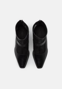 Botas negras de tobillo con punta afilada, hechas de materiales de cuero y malla, con dos bandas horizontales en la parte superior y cierre de cremallera.