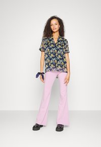 Blusa floral azul-marinho com mangas curtas, textura fofinha e decote em V. Combinada com calças pink fluídas e sapatos de plataforma pretos e robustos.