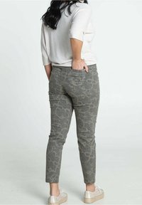 Pantalon gris à motif paisley en tissu doux. Coupe slim avec poches ; associé à un haut à manches courtes de couleur claire.