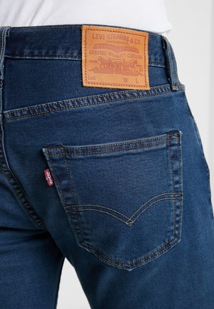 Widok z tyłu ciemnoniebieskich dżinsów Levi Strauss z widoczną tylną kieszenią, czerwoną metką i skórzaną naszywką marki na pasie.