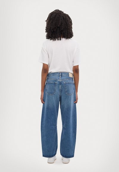 Weite Denim-Jeans in hellblau, mit hoher Taille, großen Gesäßtaschen und lockerem Schnitt. Kombiniert mit einem schlichten weißen T-Shirt.