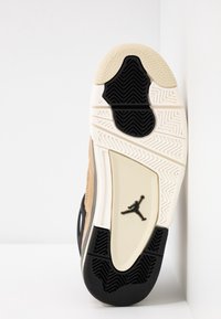 Semelle d’une basket montrant une bande de roulement noire et beige avec un petit logo Jumpman au centre sur une surface blanche.