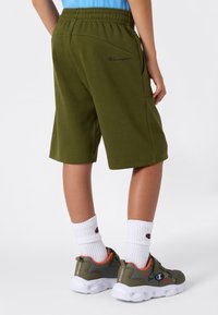 Shorts de sport verts avec une ceinture élastique et des poches latérales, associés à des baskets grises et orange ainsi qu'à des chaussettes blanches à côtes.