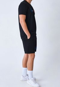 T-shirt noir avec broderie bleue et rouge, associé à un short noir avec un accent brodé, des chaussettes blanches et des baskets blanches.