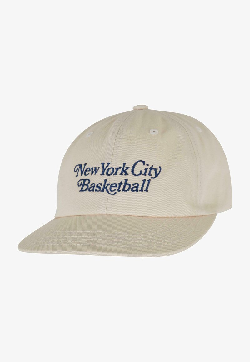 Beige baseball caps med marinblå broderte teksten "New York City Basketball" på framsiden; buet skygge og sømdetaljer.