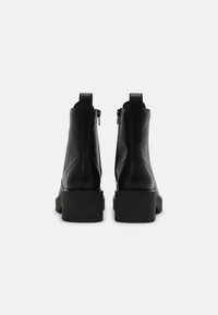 Botines de cuero negro con cierre de cremallera, tacón estriado y plataforma gruesa. Textura suave y detalles de costura mínimos.