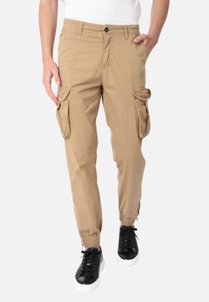 Pantaloni cargo beige con polsini elastici, molteplici tasche laterali e chiusura con bottone. Abbinati a sneakers nere con lacci.