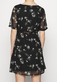 Mustakukkainen mekko läpikuultavilla hihoilla, vyötäröllä oleva vyö ja herkät valkoiset kukkakuviot. Valoisa, kevyt kangas.