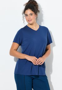 Tmavě modré tričko s výstřihem do V, krátké rukávy, vyrobené z měkké tkaniny. Má volný střih a jemné šicí detaily. Stylizováno s tmavými kalhotami.