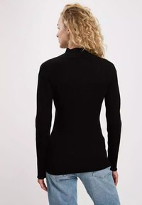 Schwarzer Rollkragenpullover mit gerippter Textur, langen Ärmeln und tailliertem Design. Getragen mit hellblauen Jeans.