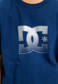 Modrá bavlněná tričko s velkým, stříbrným, tečkovaným logem a akcentovanou hvězdičkou. Klasický kulatý výstřih s krátkými rukávy.