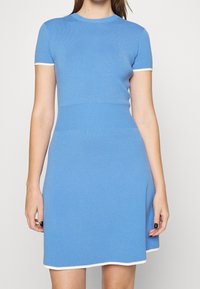 Robe courte tricotée bleue à manches courtes avec un corsage ajusté et une jupe évasée. Elle présente un col et un ourlet en côte blanche, ainsi qu'un tissu texturé.