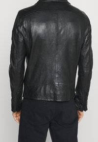 Zwarte leren jas met een klassiek ontwerp, voorzien van een puntkraag, een gladde textuur en gestikte details op de schouders en rug.