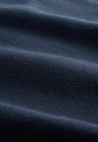 Tissu bleu marine foncé avec une surface douce et texturée, délicatement plié, mettant en valeur des motifs de tricot fins et réguliers. Apparence lisse avec un léger éclat.