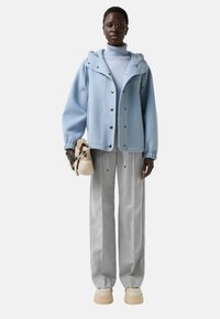 Veste en polaire bleu clair avec des boutons, pantalon large gris, et baskets à plateforme crème. Porte un petit sac beige.