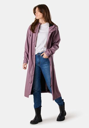 Lange, lavendelkleurige waterdichte jas met een capuchon, ritssluiting en verstelbare manchetten, gedragen over een wit shirt en blauwe jeans, gecombineerd met zwarte laarzen.