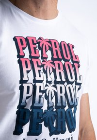 Bílý bavlněný tričko s multikolorovým nápisem "PETROL" v růžové a modré barvě, doplněné grafikou palmových stromů a zobrazujícími gradientní stínování.