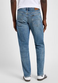 Jeans de mezclilla de color azul claro con un corte recto clásico. Bolsillos y costuras visibles. Combinados con zapatos blancos con rayas negras.