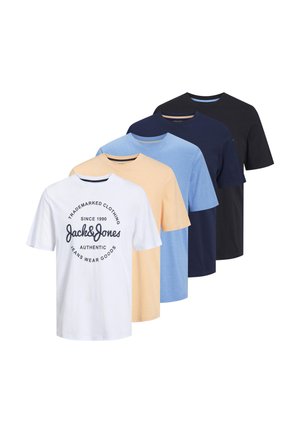 White cotton t-shirt with black circular graphic logo, paired with beige trousers and navy sneakers. Plain background, relaxed fit.