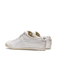White canvas sneakers with a low profile, rounded toe, and textured rubber sole; features white leather accents and silver eyelets.