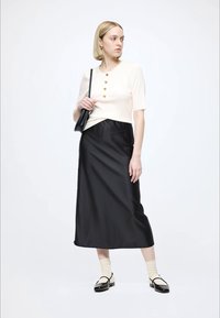 Crèmekleurige korte mouw top met ribbels en drie gouden knopen, gecombineerd met een zwarte satijnen maxi rok. Zwarte schoenen met crèmekleurige rand en sokken met patroon.