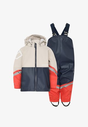 Dziecięcy kombinezon przeciwdeszczowy składający się z beżowej kurtki z granatowymi i koralowymi akcentami oraz dopasowanych granatowych spodni z elastycznymi mankietami i regulowanymi paskami.