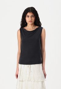 Haut sans manches noir avec un décolleté drapé et une texture lisse, associé à une jupe à volants blanche à pois.
