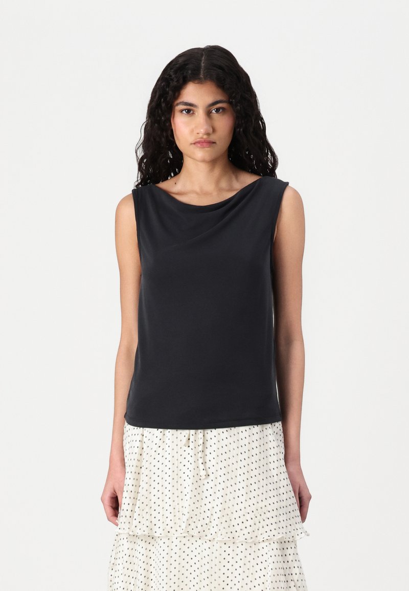 Haut sans manches noir avec un décolleté drapé et une texture lisse, associé à une jupe à volants blanche à pois.
