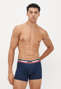 Ναυτικό μπλε σλιπάκια με μαλακό ύφασμα, με μαύρη ζώνη που έχει κόκκινες και λευκές ρίγες και το λογότυπο "Levi's".