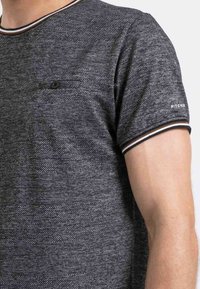 T-shirt gris texturé avec un col rond, des manches courtes, une petite poche poitrine et des accents rayés sur le col et les bords des manches.